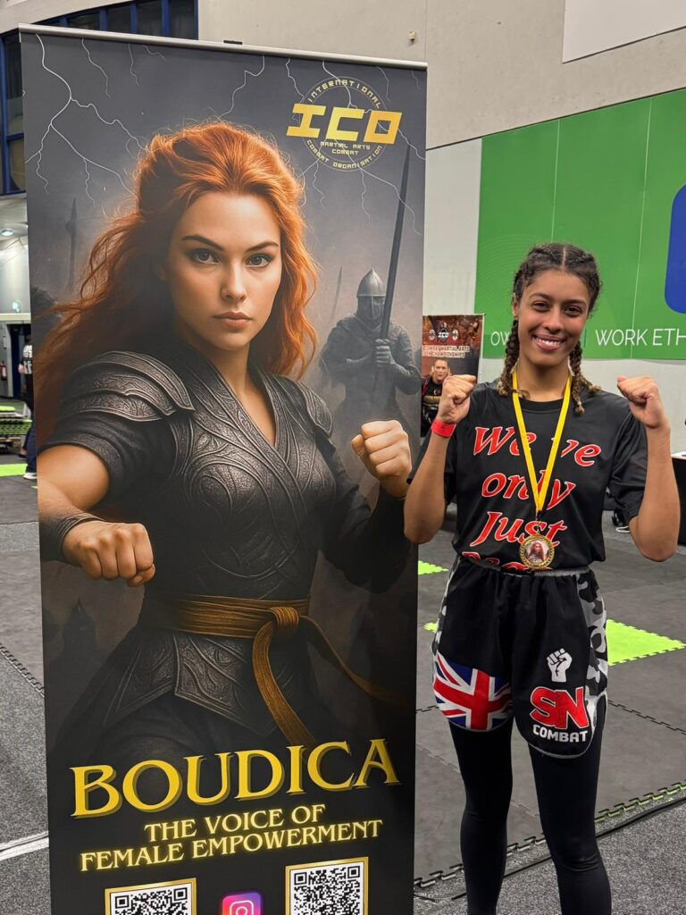 Yasmin wearing her winners medal, standing next to the ICO event poster